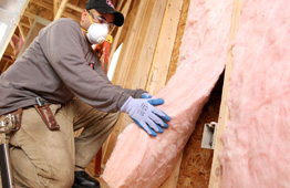 man installing fiberglass bat insulation in wall