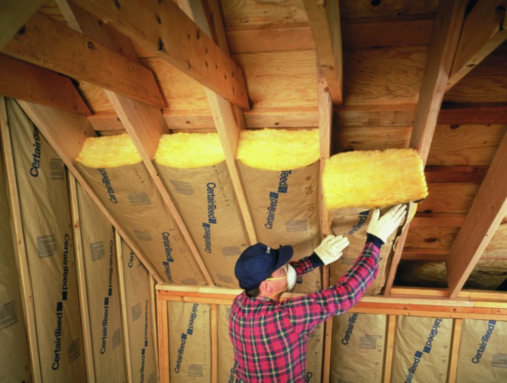 Technician installing fiberglass batt insulation in attic ceiling.