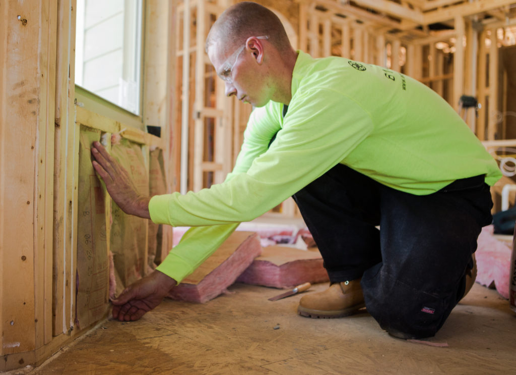 fiberglass batt insulation being rolled into wall of house